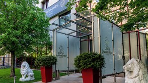A modern building with glass and metal structures, a lion statue, and a sign for "Lion's Garden Hotel." - Lions Garden Hotel (Budapest)