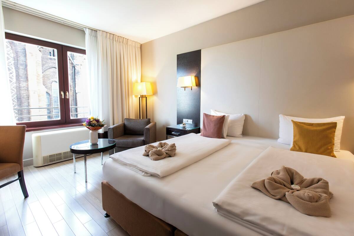 Hotellihuone, jossa on suuri sänky, tuoli, pieni pöytä ja ikkuna, jossa on verhot.