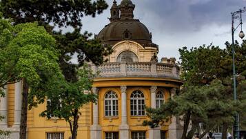 A historic building with a prominent dome and classical architecture, surrounded by trees and a pathway.