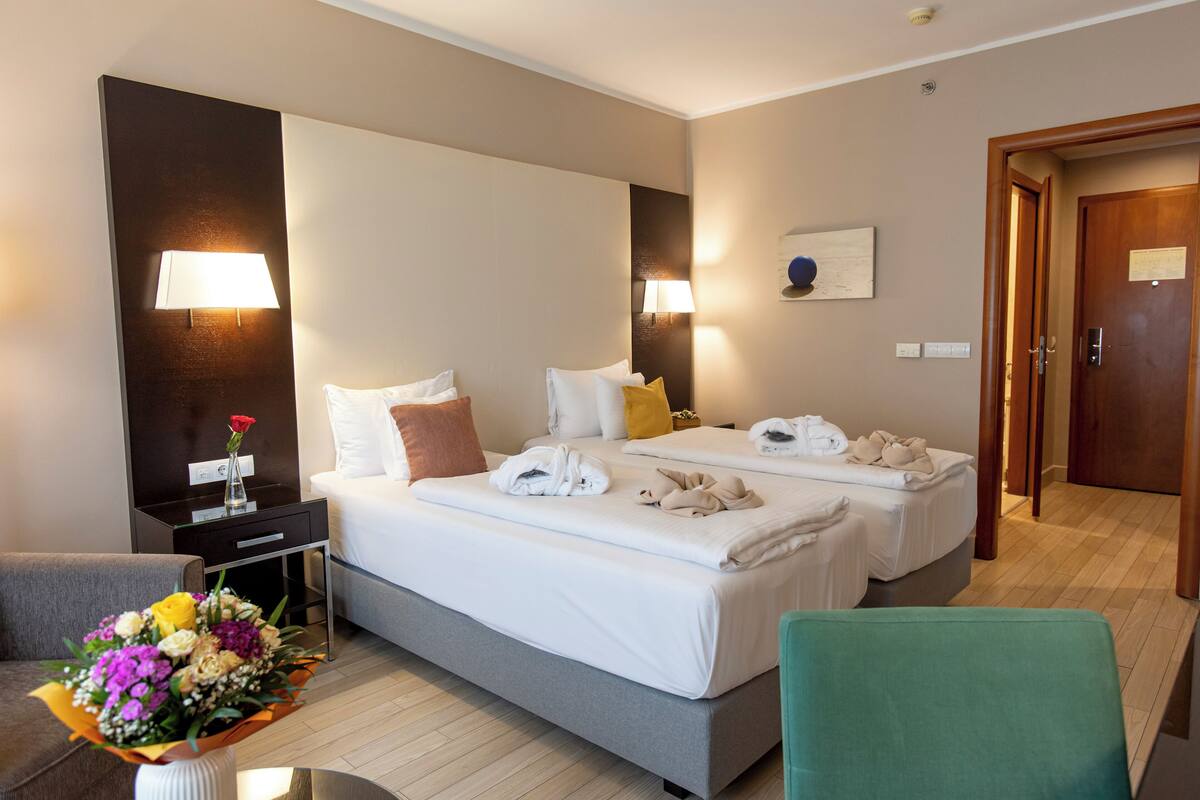 Hotellihuone, jossa on kaksi sänkyä, työpöytä, tuoli ja maljakko kukkineen.