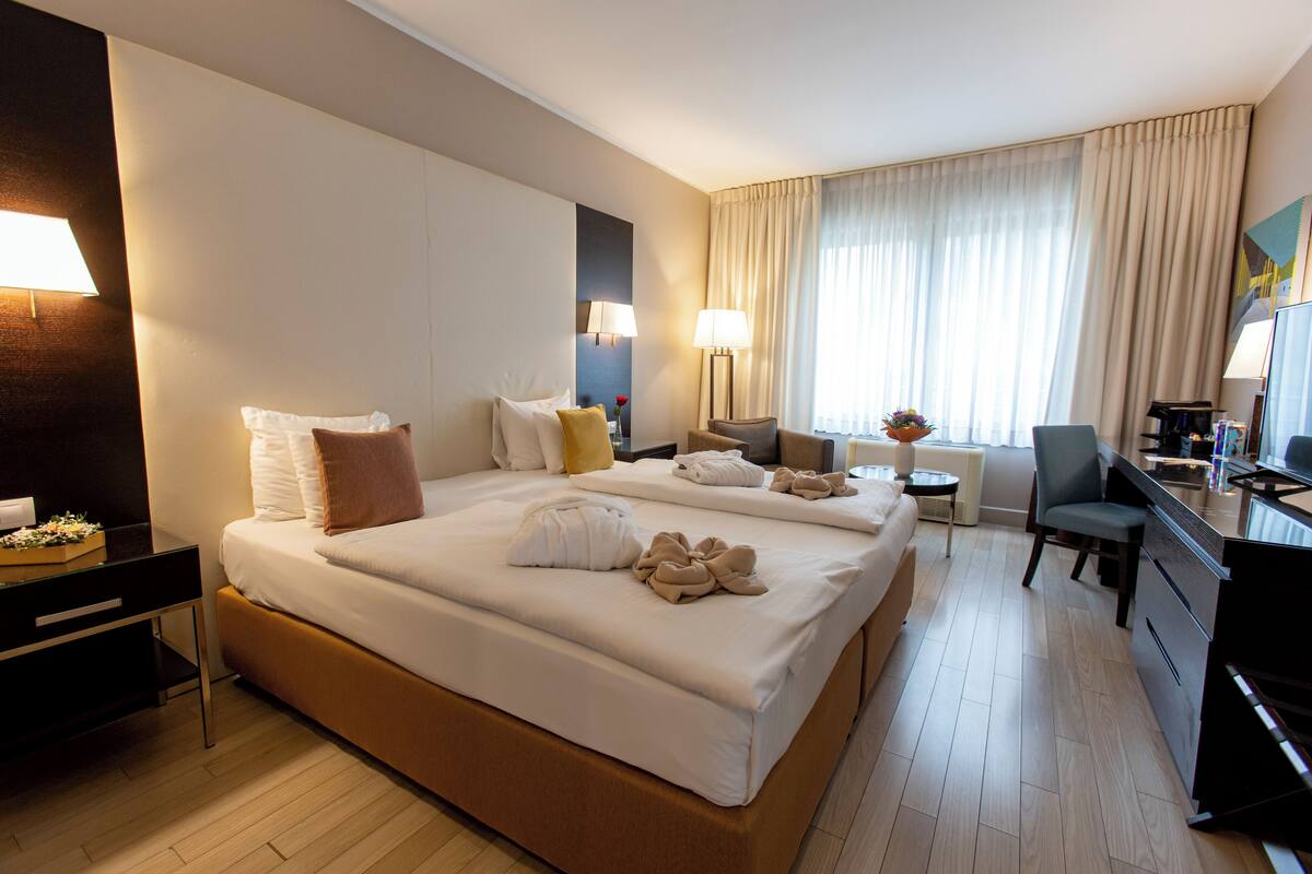 Hotellihuone, jossa on suuri sänky, työpöytä, tuoli ja pieni pöytä, jossa on lamppu.
