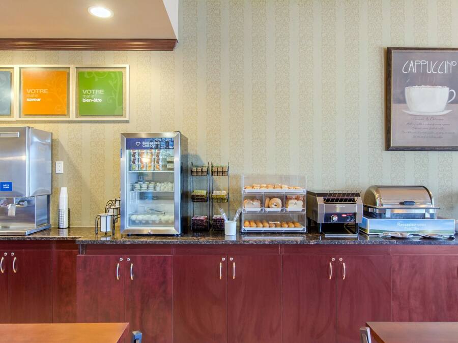 A breakfast bar with a coffee machine, a refrigerator, and a display case with pastries.