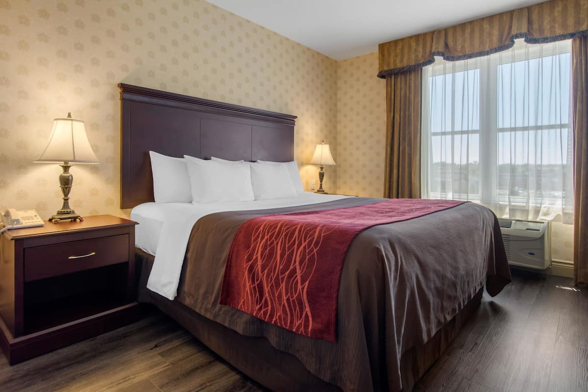 A hotel room with a large bed, two bedside tables with lamps, a window with curtains, and a patterned wallpaper.