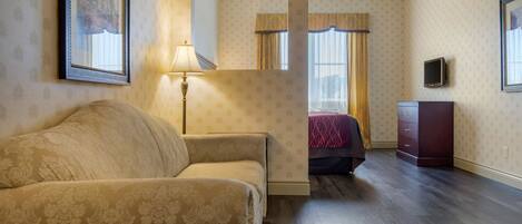 A hotel room with a sofa, a lamp, a TV, a dresser, and a bed with curtains.