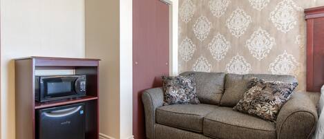 A compact living space with a kitchenette, a sofa with patterned cushions, and a patterned wallpaper wall.