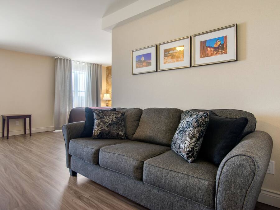 A living room with a grey sofa, two framed pictures on the wall, a small table, and a lamp.