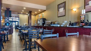 Un restaurant avec des tables et des chaises, un comptoir avec des machines à café et un mur orné d’un panneau représentant une tasse de café.