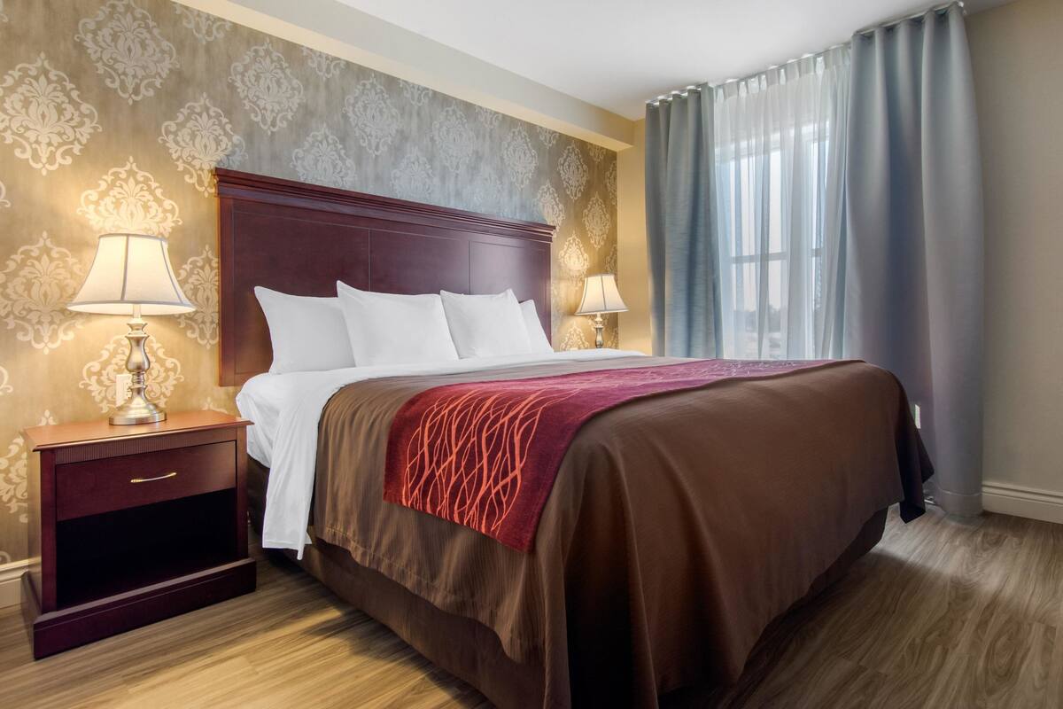 A hotel room with a large bed, two bedside tables with lamps, a red throw blanket, and patterned wallpaper.