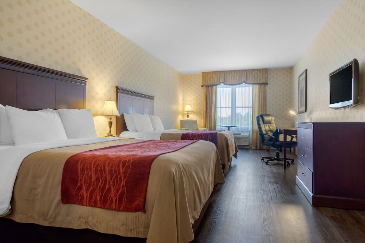 A hotel room with two beds, a desk, a chair, a television, and a dresser.