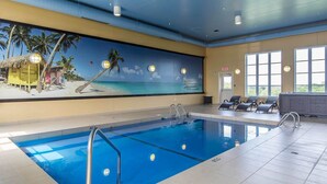 Une piscine intérieure ornée d’une fresque représentant une scène de plage, avec des chaises longues et un espace sauna.
