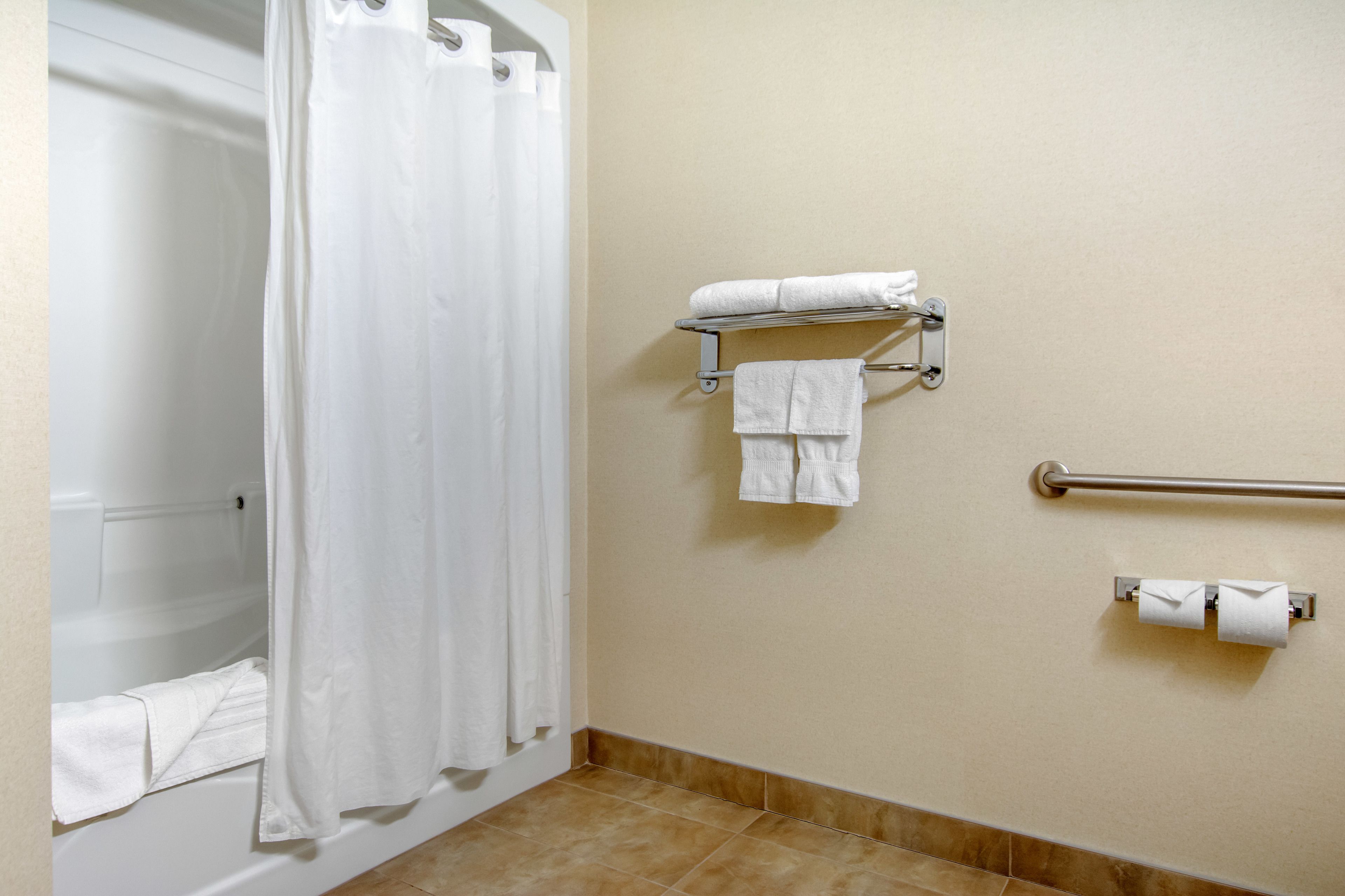 A bathroom with a bathtub, a shower curtain, a towel rack with towels, a grab bar, and toilet paper.