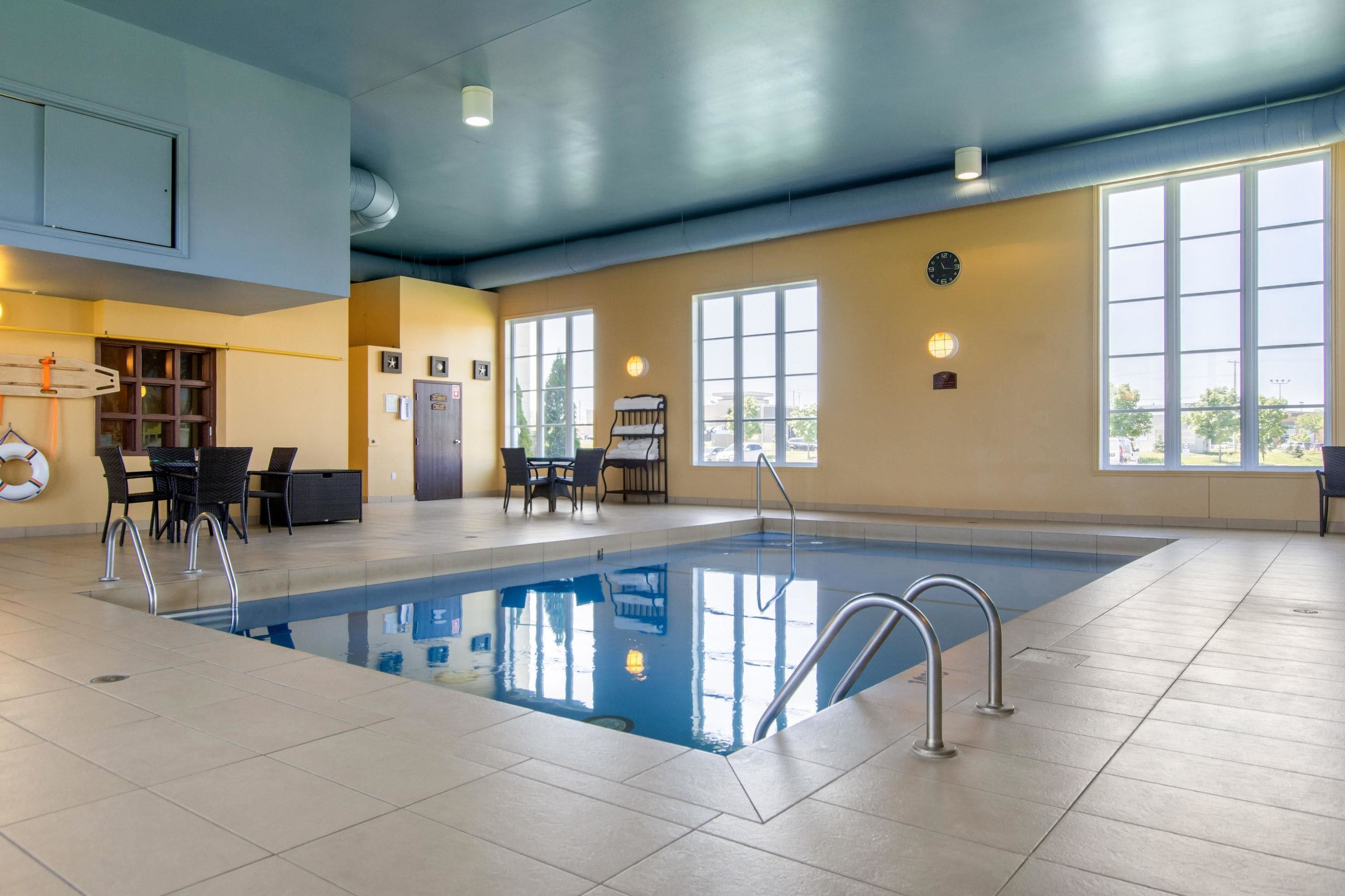 Una piscina interior con agua cristalina, rodeada de suelo de baldosas y equipada con barandillas de metal.