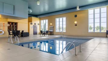 Una piscina interior con agua cristalina, rodeada de suelo de baldosas y equipada con barandillas de metal.