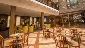 A spacious lobby with multiple seating areas, including round tables and chairs, and a bar area with shelves of bottles. - Daugirdas Hotel (Kaunas)