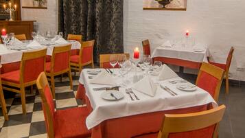 Un restaurant dont le sol est recouvert de carreaux, avec des chaises en bois dotées de coussins rouges et des tables nappées de nappes blanches.