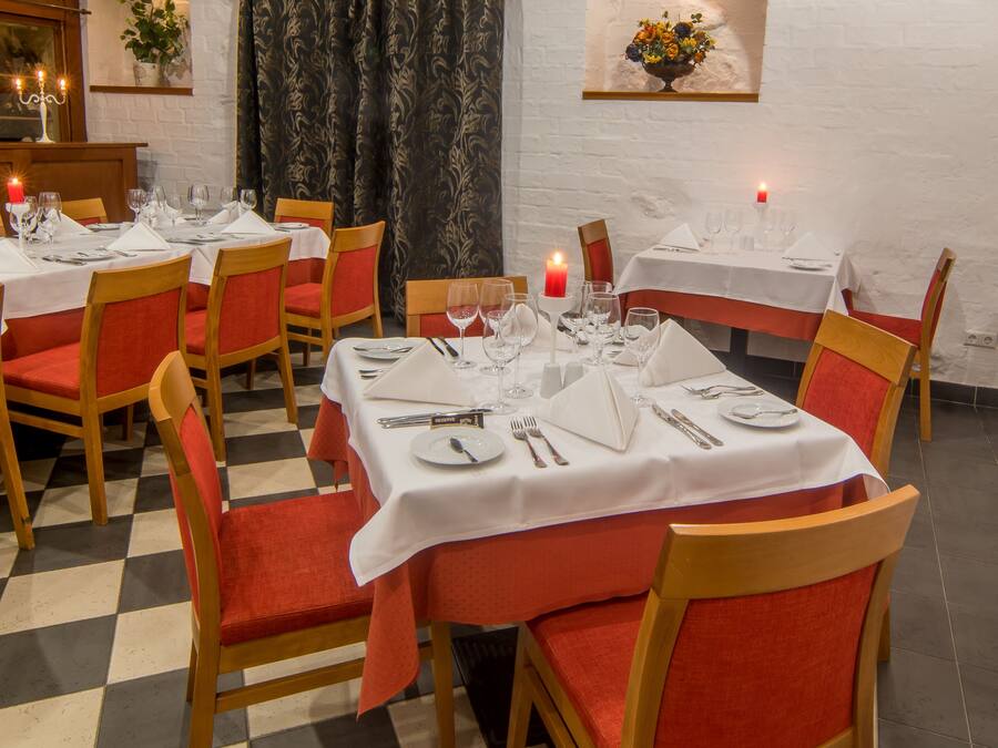 Un restaurant dont le sol est recouvert de carreaux, avec des chaises en bois dotées de coussins rouges et des tables nappées de nappes blanches.