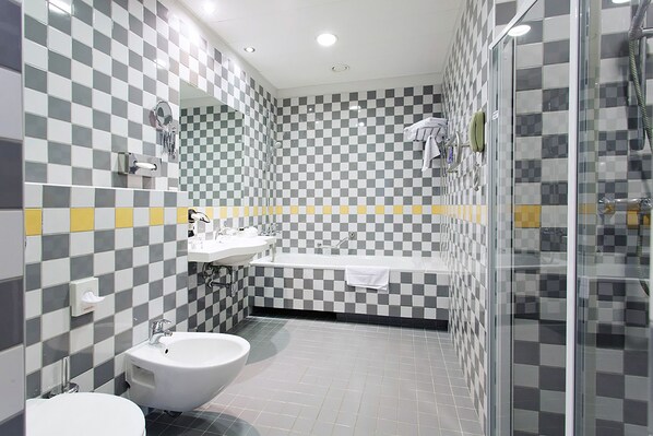 A bathroom with a checkered tile wall, a sink, a bidet, and a glass-enclosed shower area.