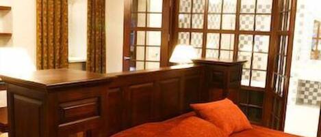 Una habitación con una cama de madera, un escritorio y un ventanal con vidrieras decorativas.