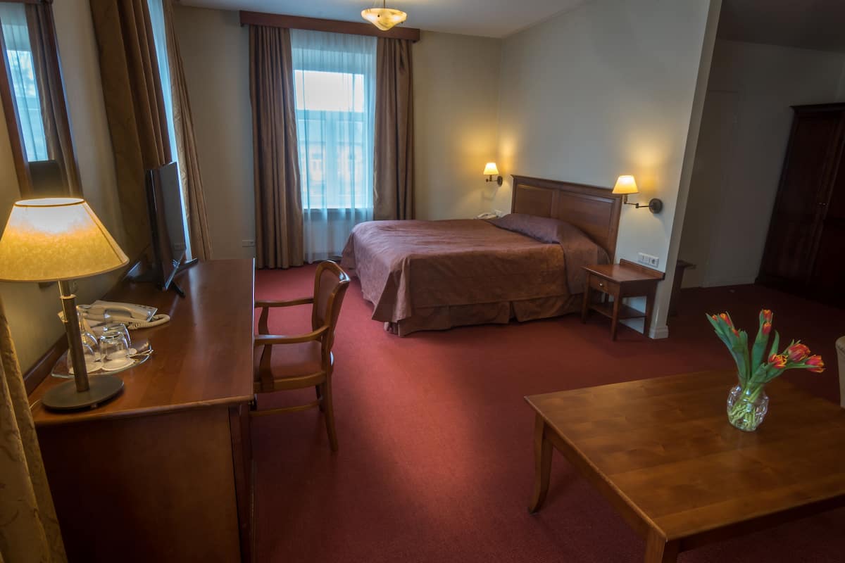 Ein Hotelzimmer mit Bett, Nachttische, Schreibtisch, Stuhl, Lampe und einer Vase mit Blumen.