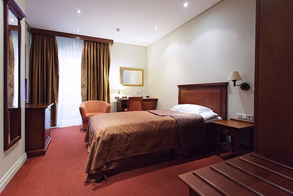 A hotel room with a bed, a desk, a chair, a wardrobe, and a mirror.