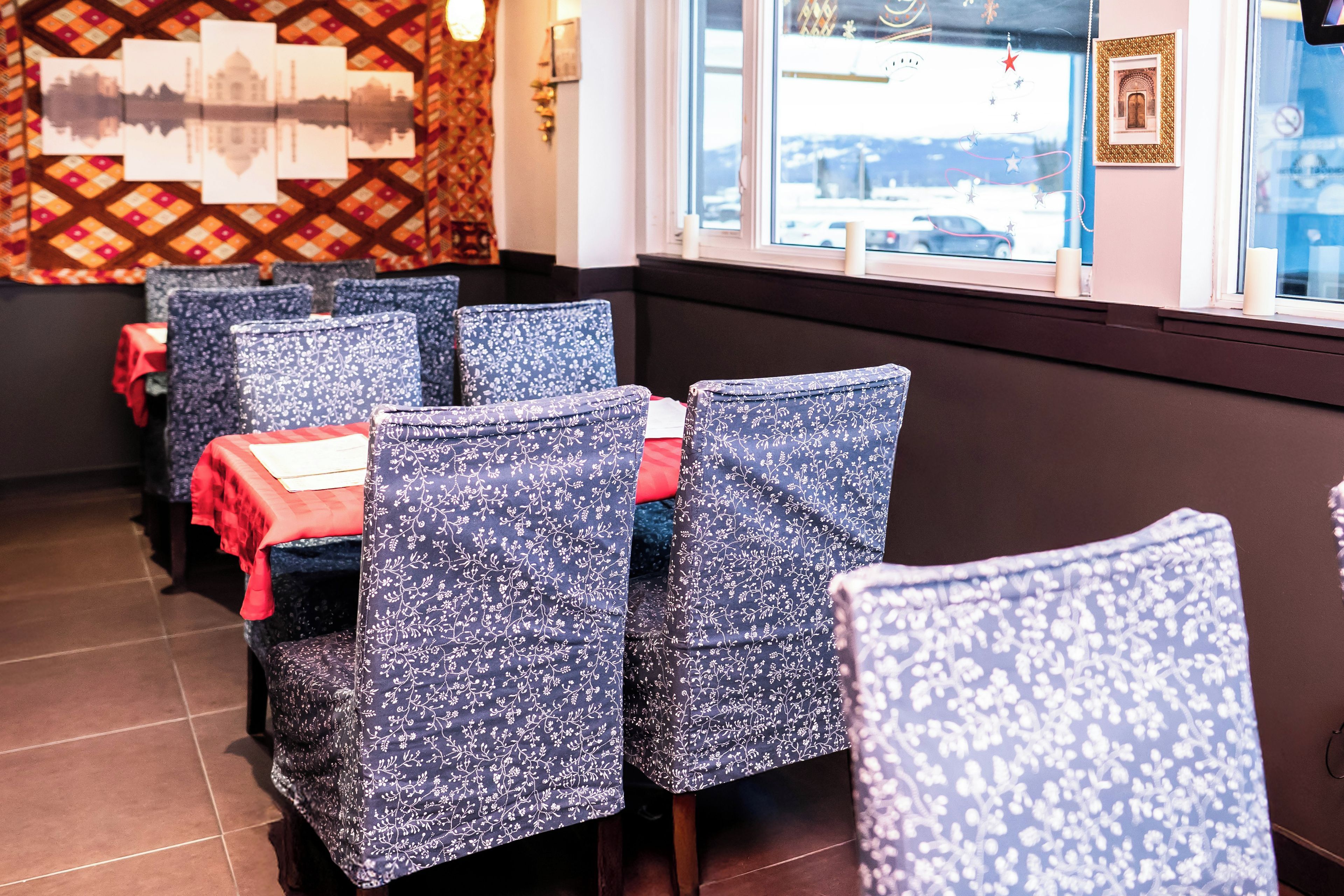 A restaurant interior with tables and chairs, a patterned wall, and a window with a view.