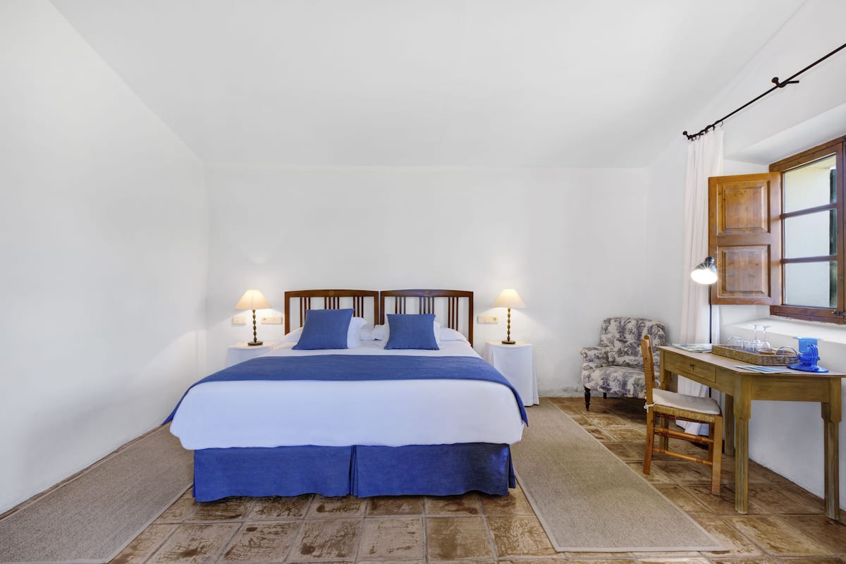 A bedroom with a bed, bedside lamps, a chair, a desk, and a mirror.