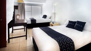 A hotel room with a bed, bedside table, lamp, and a desk with a chair.