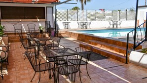 An outdoor patio with metal tables and chairs, a pool, and a white fence.
