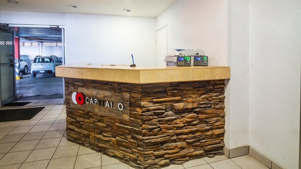 A reception desk with a stone facade, a sign reading "CAPITALO", and a parking area visible through the door.