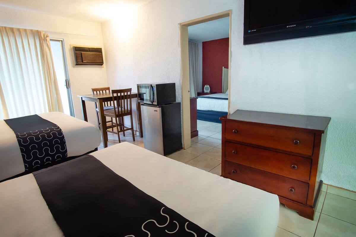 Quarto de hotel com cama, escrivaninha com computador, televisão e cômoda.
