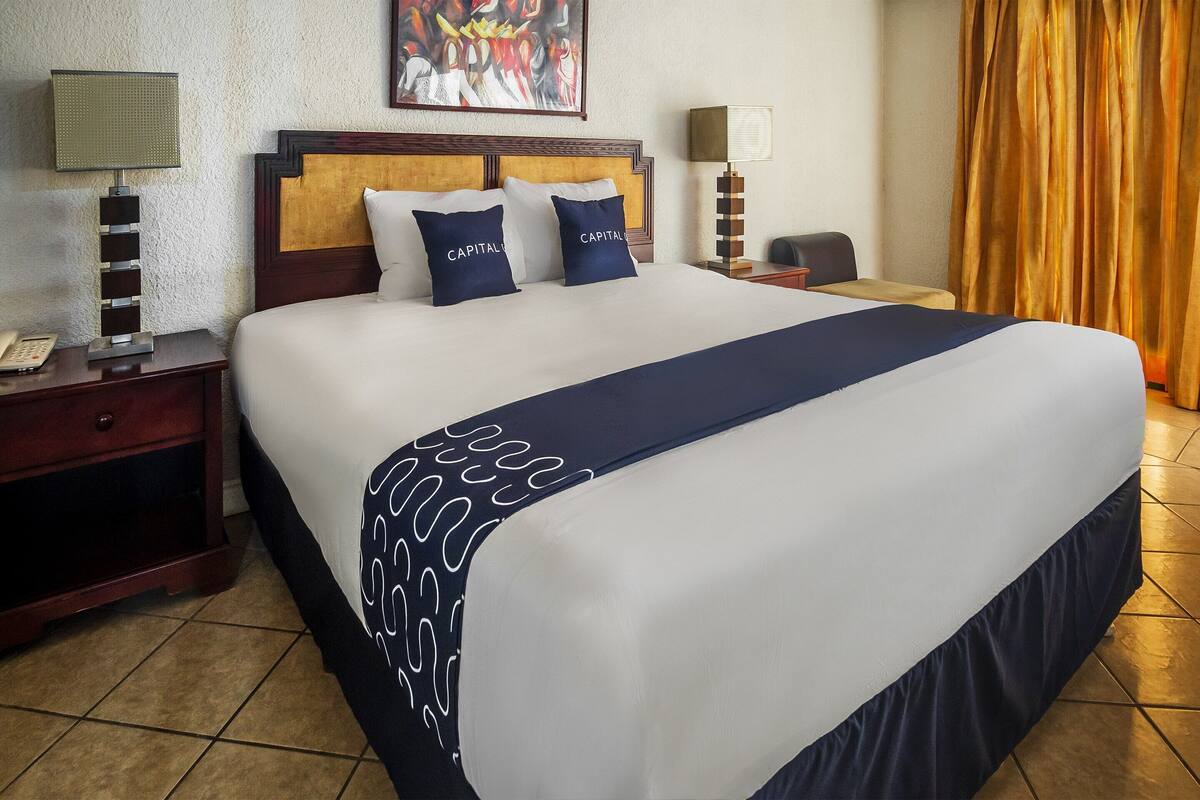 Quarto de hotel com uma cama grande, duas mesas de cabeceira, uma escrivaninha, uma cadeira e um quadro na parede.