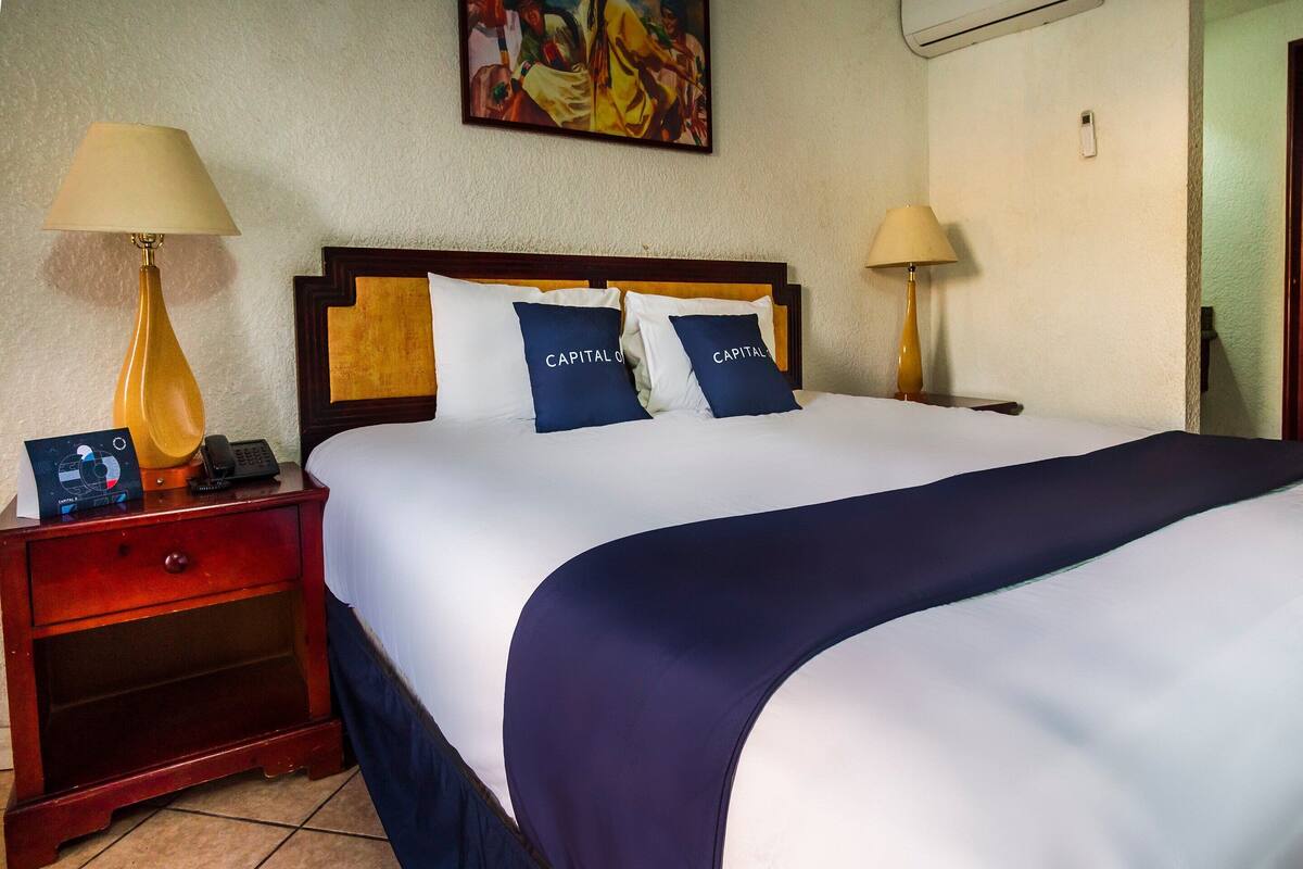 Quarto de hotel com uma cama grande, duas mesas de cabeceira, um quadro na parede e um telefone na mesa de cabeceira.