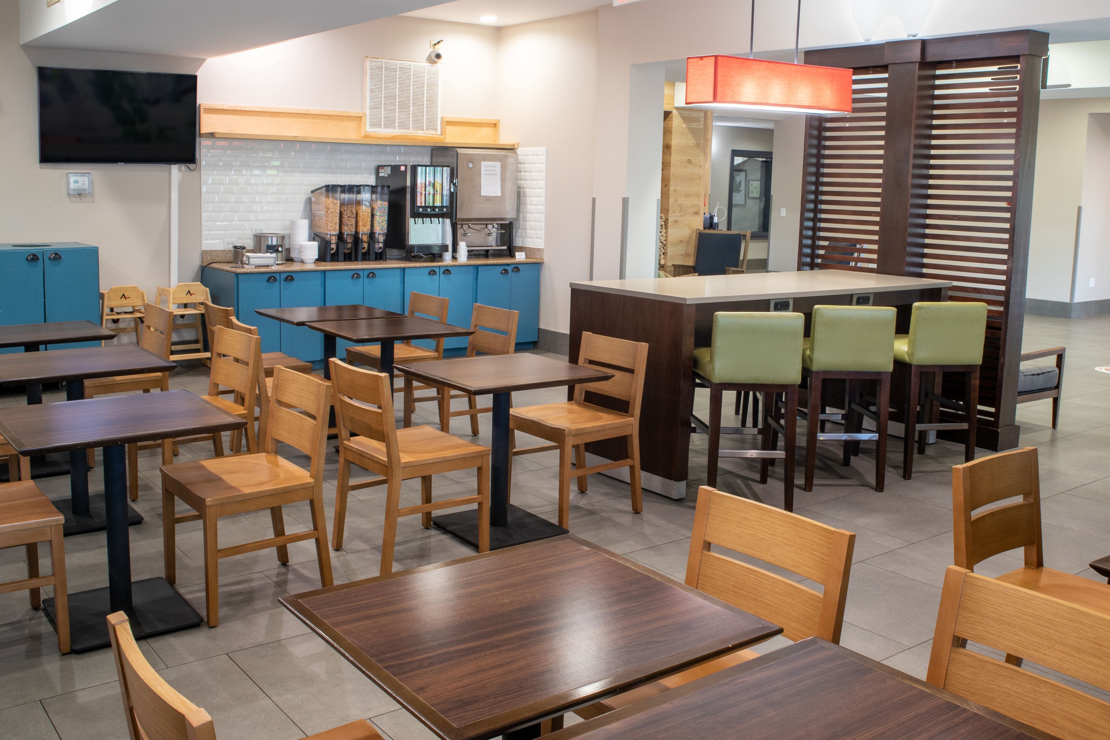 Ein Restaurant mit Holztischen und -stühlen, einem Küchenbereich mit einer Kaffeemaschine und einer Theke mit einer roten Lampe.