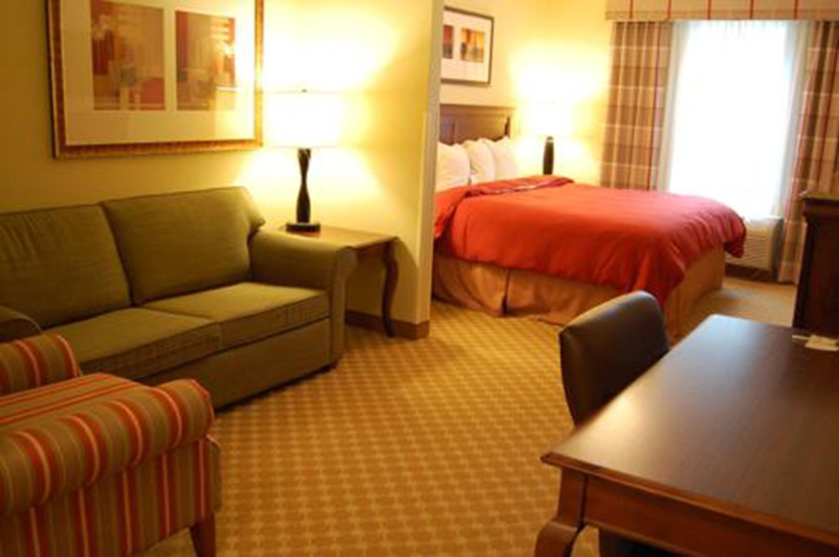 A hotel room with a bed, a sofa, a small table, and a lamp.
