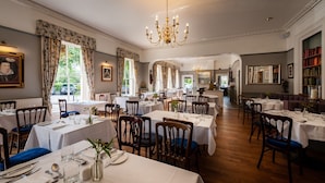 A formal dining room with multiple tables set for service, a chandelier, and framed artwork on the walls. - Old Hall Hotel (Buxton)
