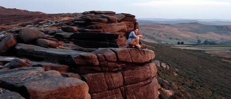 A person sitting on a rocky outcrop with a view of rolling hills in the background.