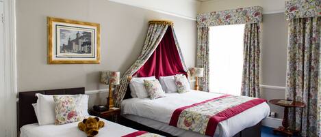A double bed with floral bedding, a nightstand with a lamp, a teddy bear, and a framed picture on the wall.