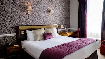 A neatly made bed with a headboard, a bedside table with a lamp, and a nightstand with a telephone.