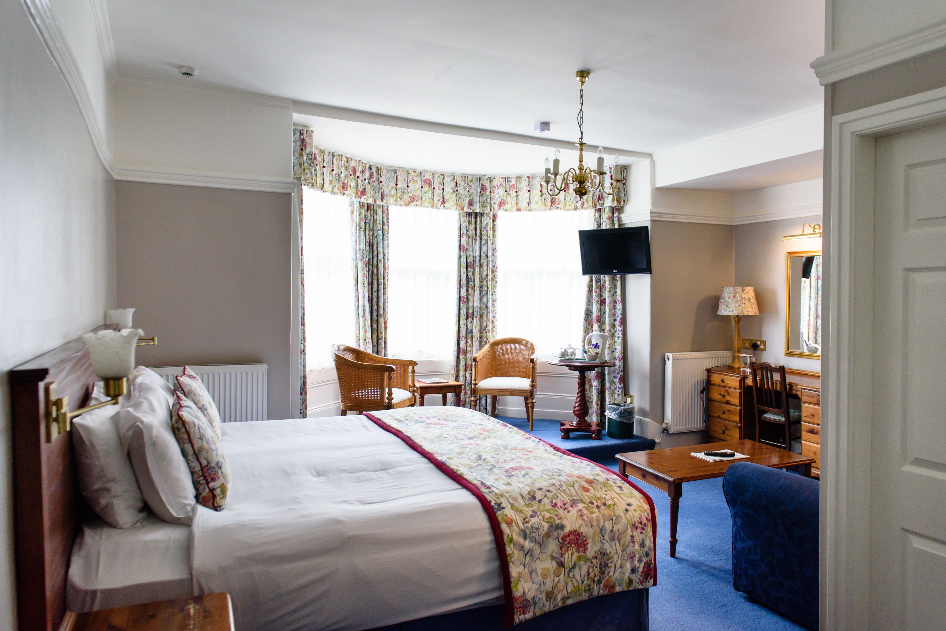 A hotel room with a large bed, a desk, a chair, a television, and a window with curtains.