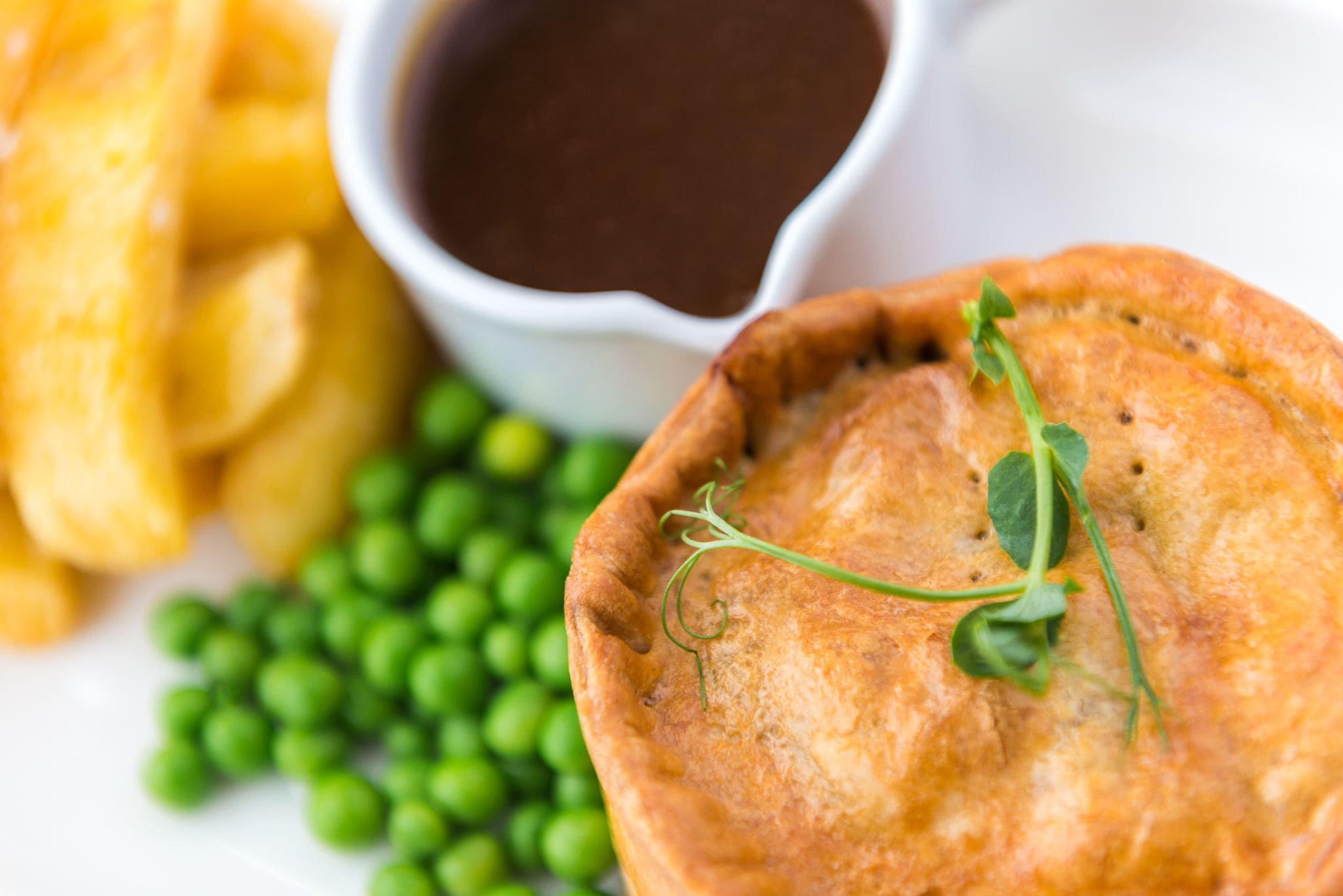 A food dish with peas, a small bowl of sauce, and a side of fries.