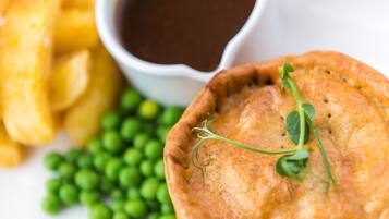 A food dish with peas, a small bowl of sauce, and a side of fries.