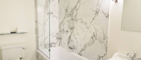 A bathroom with a marble wall, a bathtub, a toilet, and a sink.