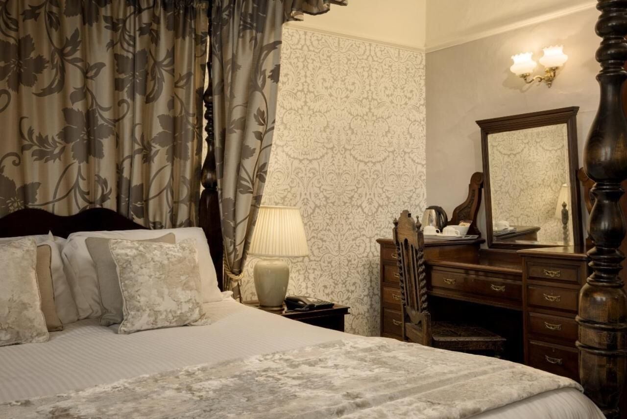 A neatly made bed with a patterned bedspread, a bedside lamp, a dresser with a mirror, and floral curtains.