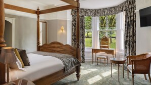 A four-poster bed with a wooden headboard, a bedside table with a lamp, a chair, and a small table. - Old Hall Hotel (Buxton)