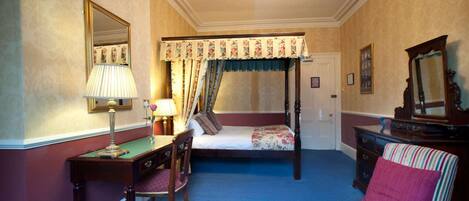 A bedroom with a four-poster bed, a desk with a lamp, a chair, a dresser, and a striped armchair.