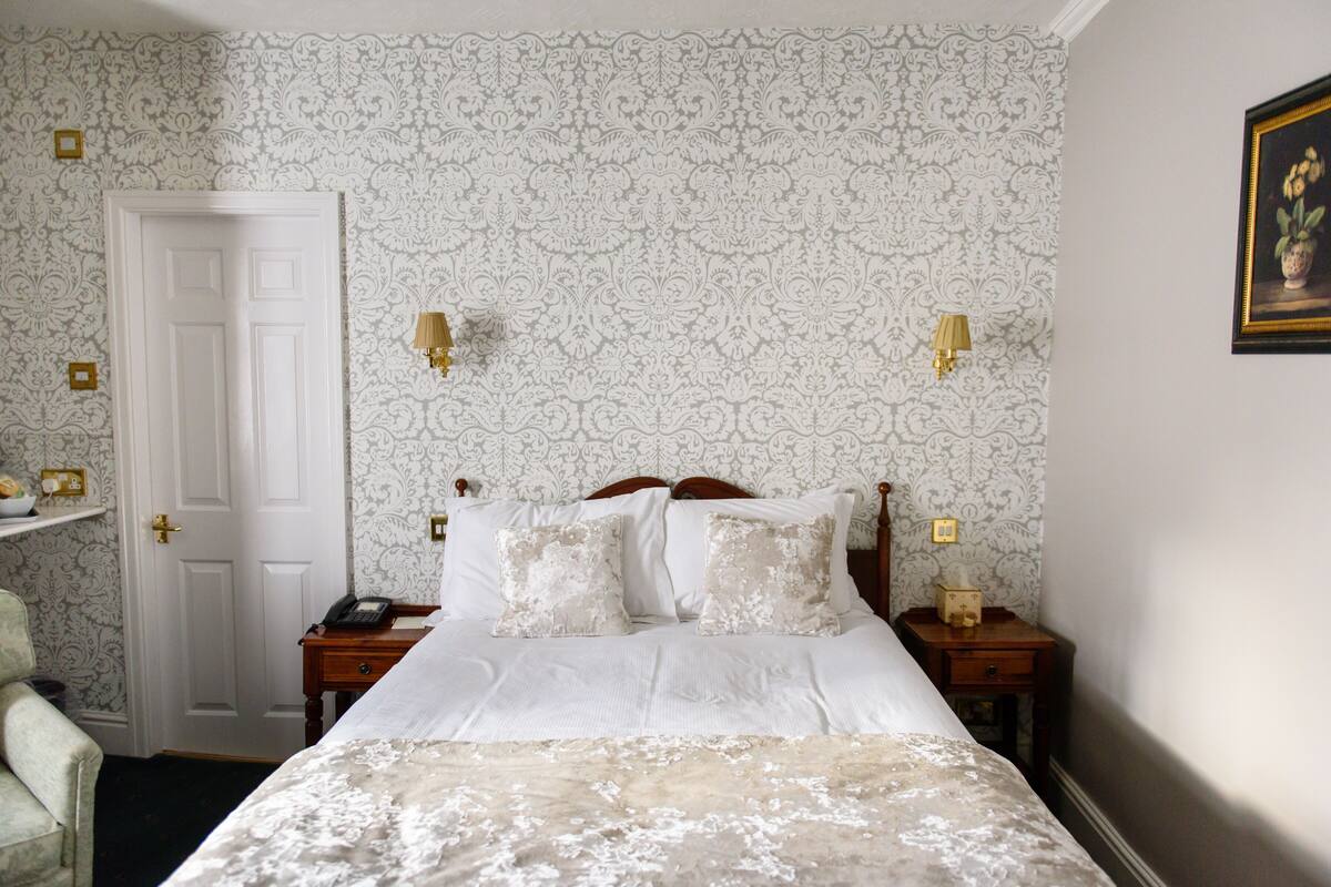 A bedroom with a bed, two bedside tables, a nightstand, a chair, and a door.