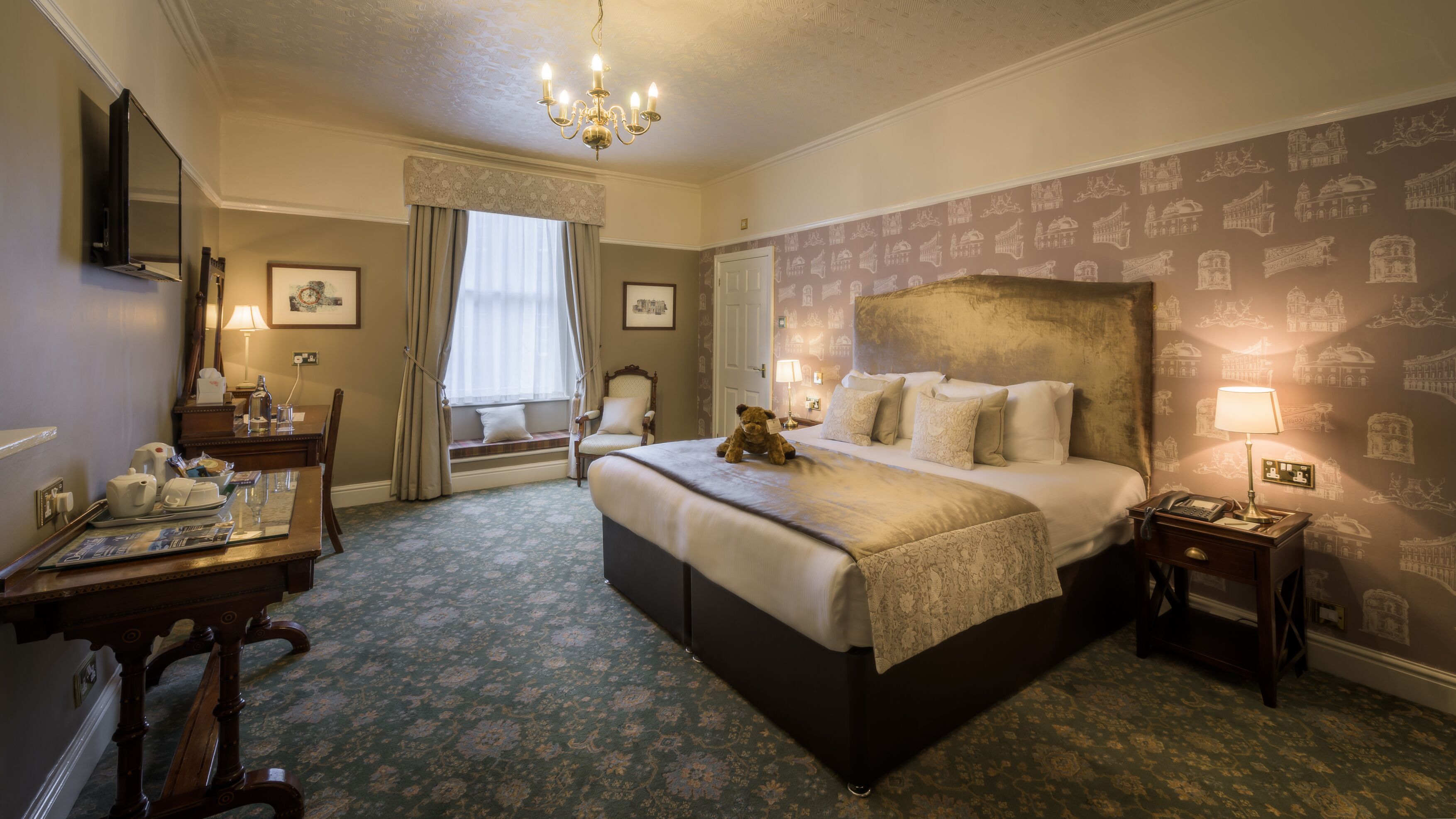 Une chambre d’hôtel avec un grand lit, un bureau avec une chaise, une table de chevet avec une lampe et une fenêtre avec des rideaux.