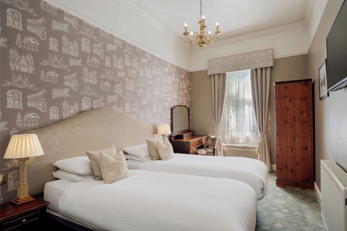 A hotel room with two beds, a wooden dresser, a vanity with a mirror, and a chandelier.