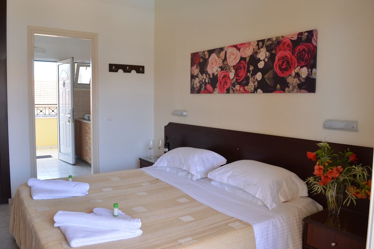 A hotel room with a bed, a nightstand, a vase with flowers, and a painting on the wall.