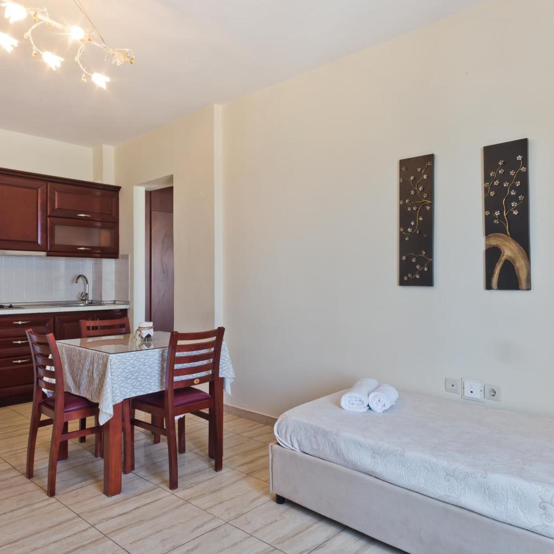 Un dormitorio con una cama, una mesa de comedor con sillas, una zona de cocina con armarios y dos cuadros colgados en la pared.